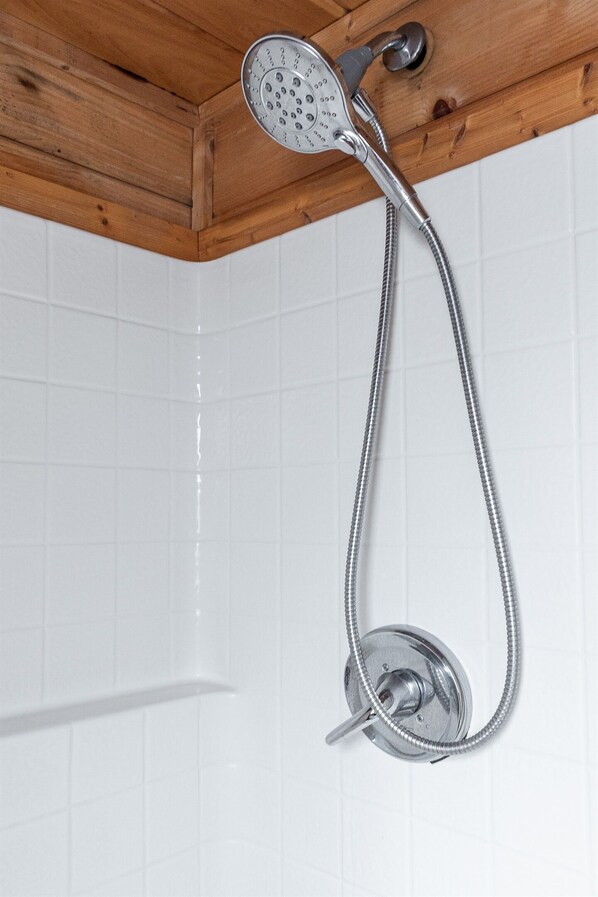 Un pommeau de douche doté d’un flexible, fixé au plafond en bois, devant un mur carrelé.