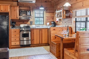 A wooden cabin kitchen with a stove, oven, microwave, and a coffee maker.