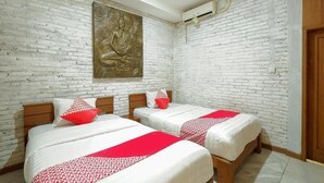 Une chambre avec deux lits, des murs en briques blanches et une grande statue de Bouddha.