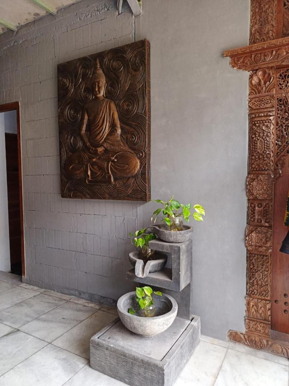 Una habitación con una estatua de Buda, una jardinera de piedra con plantas y una estructura de madera tallada.
