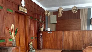 Un espace d’accueil doté d’un comptoir de réception en bois, d’une horloge, d’un ventilateur de plafond et de luminaires sphériques suspendus.