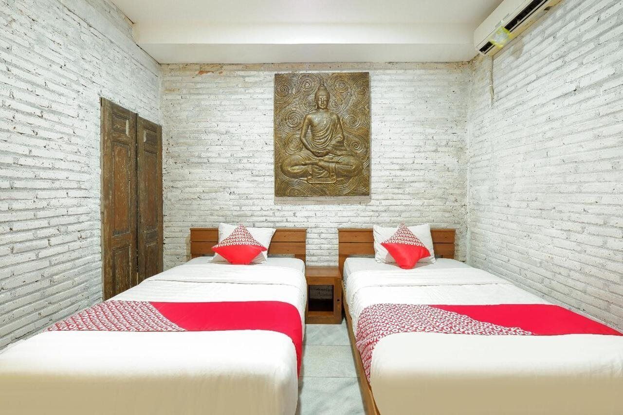 Ein Zimmer mit zwei Betten, weißen Ziegelwänden, einer Holztür und einer Buddha-Statue an der Wand.