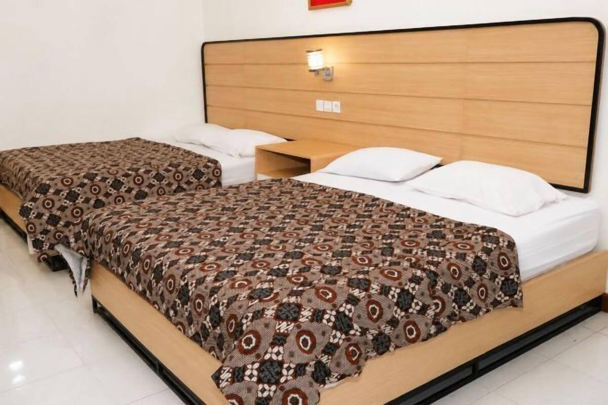 Ein Doppelbett mit gemustertem Bettbezug, einem Holzkopfstück und einem Nachttisch mit Lampe.