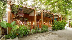 Un espace extérieur abrité, doté d’un sol en béton et entouré de différentes plantes ainsi que d’une cage à oiseaux.