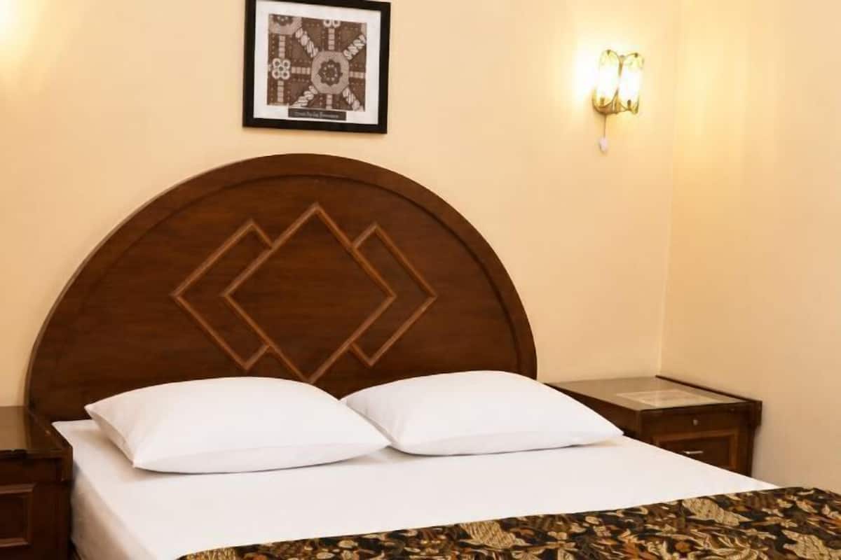 Ein ordentlich bezogenes Bett mit einem Holz-Kopfteil, ein gerahmtes Bild an der Wand und eine wandmontierte Leuchte.