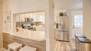 A modern kitchen with a large island, stainless steel appliances, and a wooden accent wall. - Modern Townhome- Walk to Brewery (Woodstock)