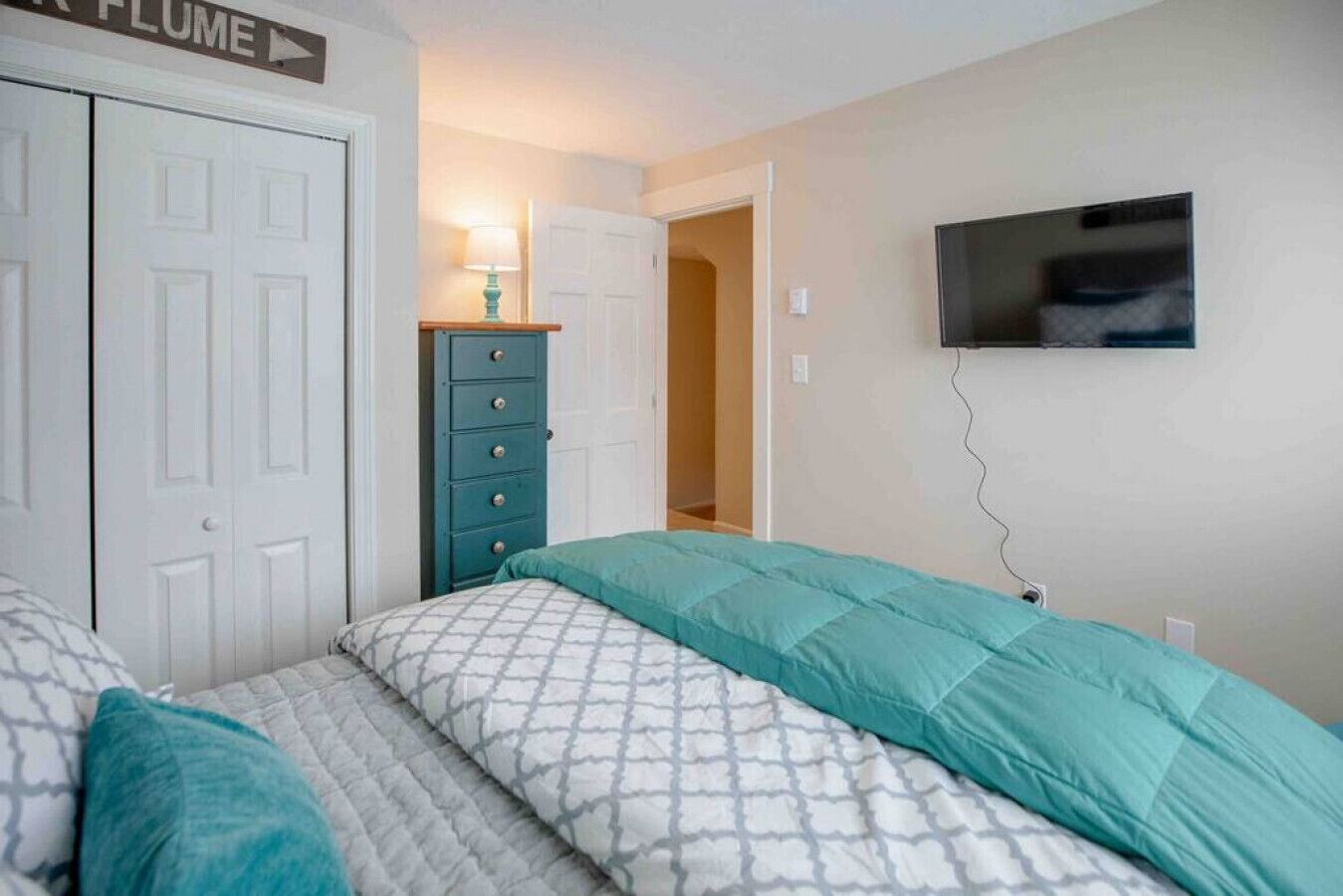 Een slaapkamer met een bed, een dressoir, een televisie en een deur met de tekst 'FLUME'.