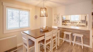 A modern kitchen with a wooden table, white chairs, and a hanging light fixture. - Modern Townhome- Walk to Brewery (Woodstock)