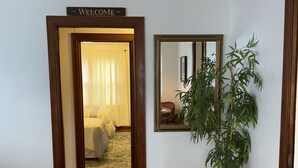A hallway with a wooden floor, a welcome sign, a mirror, and a potted plant. - Charming Ranch style house across from Mercyhurst University (Erie)