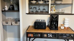 A kitchen with a wooden table, a coffee maker, a toaster, and various kitchenware. - Charming Ranch style house across from Mercyhurst University (Erie)