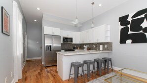 A modern kitchen with white cabinets, a stainless steel refrigerator, and a central island with bar stools. - Feng shui Philly Townhouse Unit w Rooftop (Philadelphia)