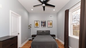 A bedroom with a bed, nightstands, a dresser, a ceiling fan, a window with curtains, and wall art. - Feng shui Philly Townhouse Unit w Rooftop (Philadelphia)