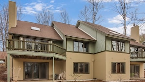 Une maison à deux étages, avec une façade verte, de grandes fenêtres et un patio couvert.