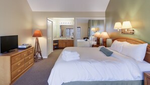 Une chambre d’hôtel avec un grand lit, une télévision, une commode, une lampe et une salle de bain visible à travers une porte ouverte.