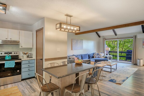 A modern kitchen with a central island, dining chairs, and a hanging light fixture.