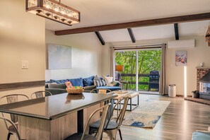 A modern kitchen with a central island, dining chairs, and a large window overlooking a deck.