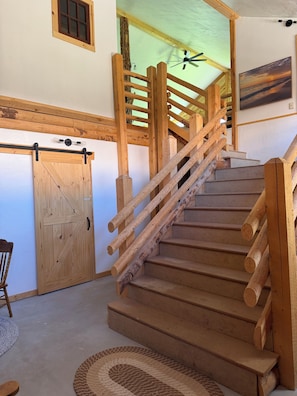 Eine Holztreppe mit Geländer, eine Holztür und ein Deckenventilator.