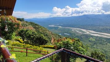 A scenic view from a balcony overlooking a river valley with lush greenery and distant mountains.