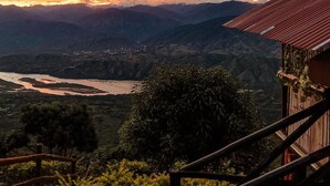 A mountainous landscape with a river, a wooden structure with a red roof, and a wooden fence. - Glamping Mirador de Santa Fe  (Sopetrán)