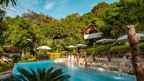 A pool area with a wooden deck, umbrellas, and a waterfall feature. - Glamping Mirador de Santa Fe  (Sopetrán)