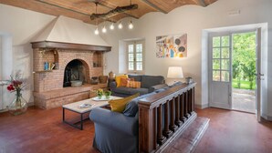 A cozy living room with a brick fireplace, a sofa, a coffee table, and a view of the outdoors through a door. - Villa in Gambassi with pool, A/C, village and restaurant at walking distance, (Gambassi Terme)