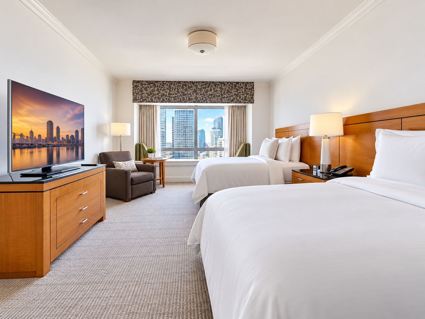 Een hotelkamer met twee bedden, een bureau, een flatscreen-televisie, een stoel, een nachtkastje met lamp en een raam met uitzicht op de stad.