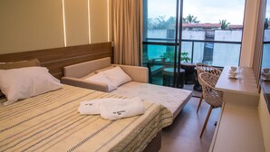 A hotel room with a bed, a sofa, a dining table, and a balcony with a view of the city. - Villa del Porto (Ipojuca)