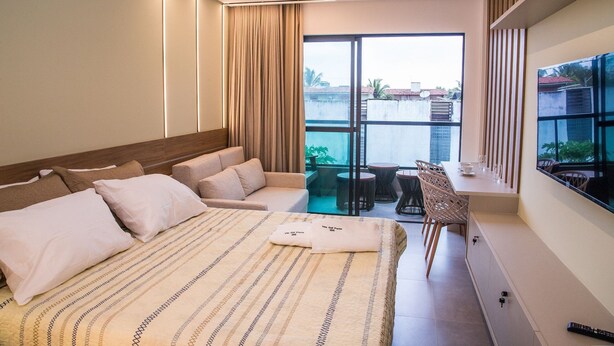 A modern bedroom with a large bed, a sofa, a dining area, and a balcony with a view. - Villa del Porto (Ipojuca)