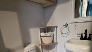 A bathroom with a toilet, a shelf with towels, a sink, and a mirror. - Tranquilo y Comodo. (Compton)