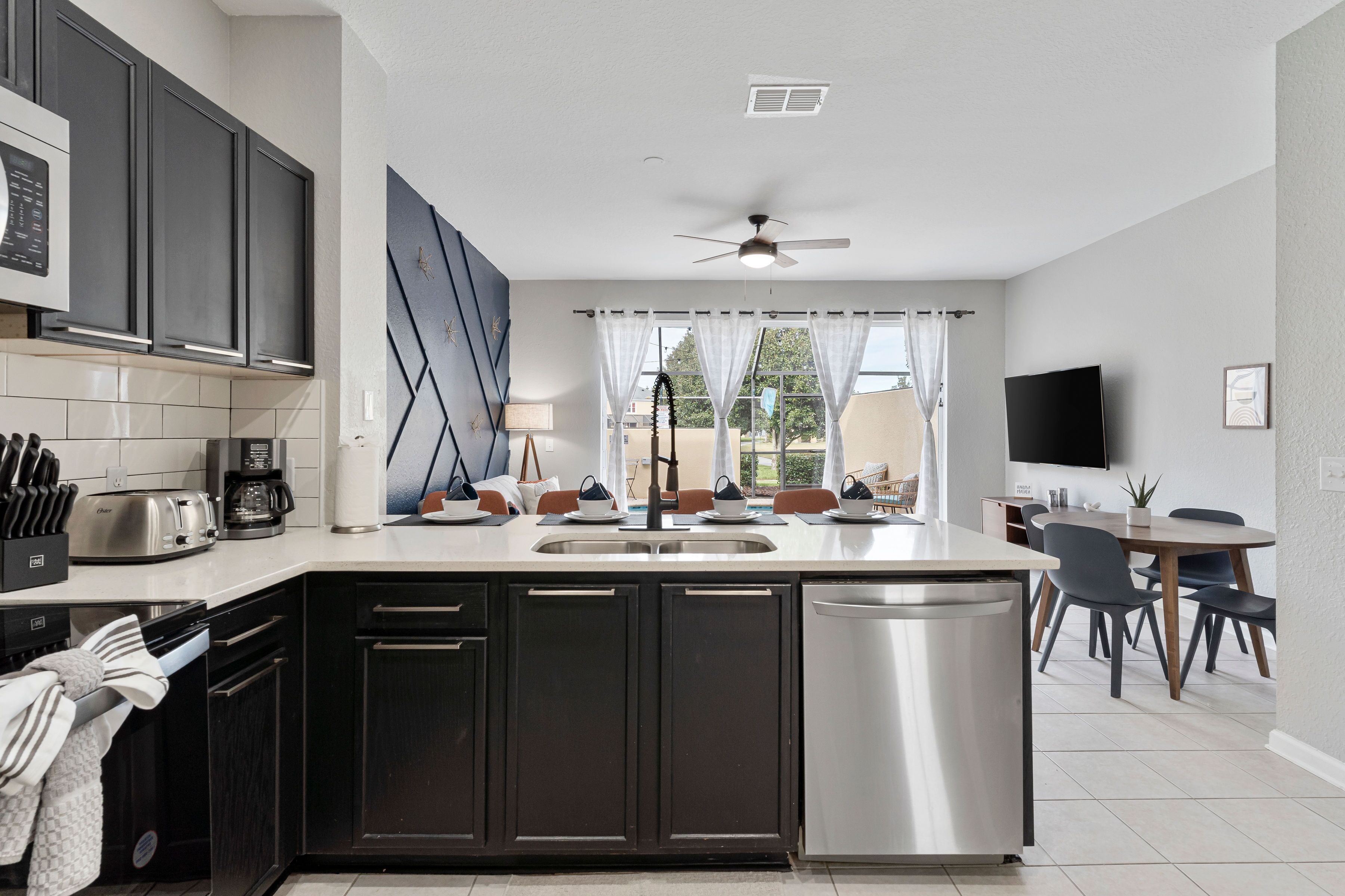 A modern kitchen with dark cabinets, a stainless steel dishwasher, and a dining area with a table and chairs.