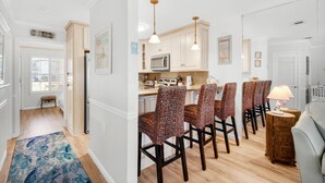 A modern kitchen with white cabinets, a microwave, and a dining area with wicker chairs. - ⭐350 yards to Beach~First Floor~Community Pool~1BR Sandprints A3⭐ (Miramar Beach)