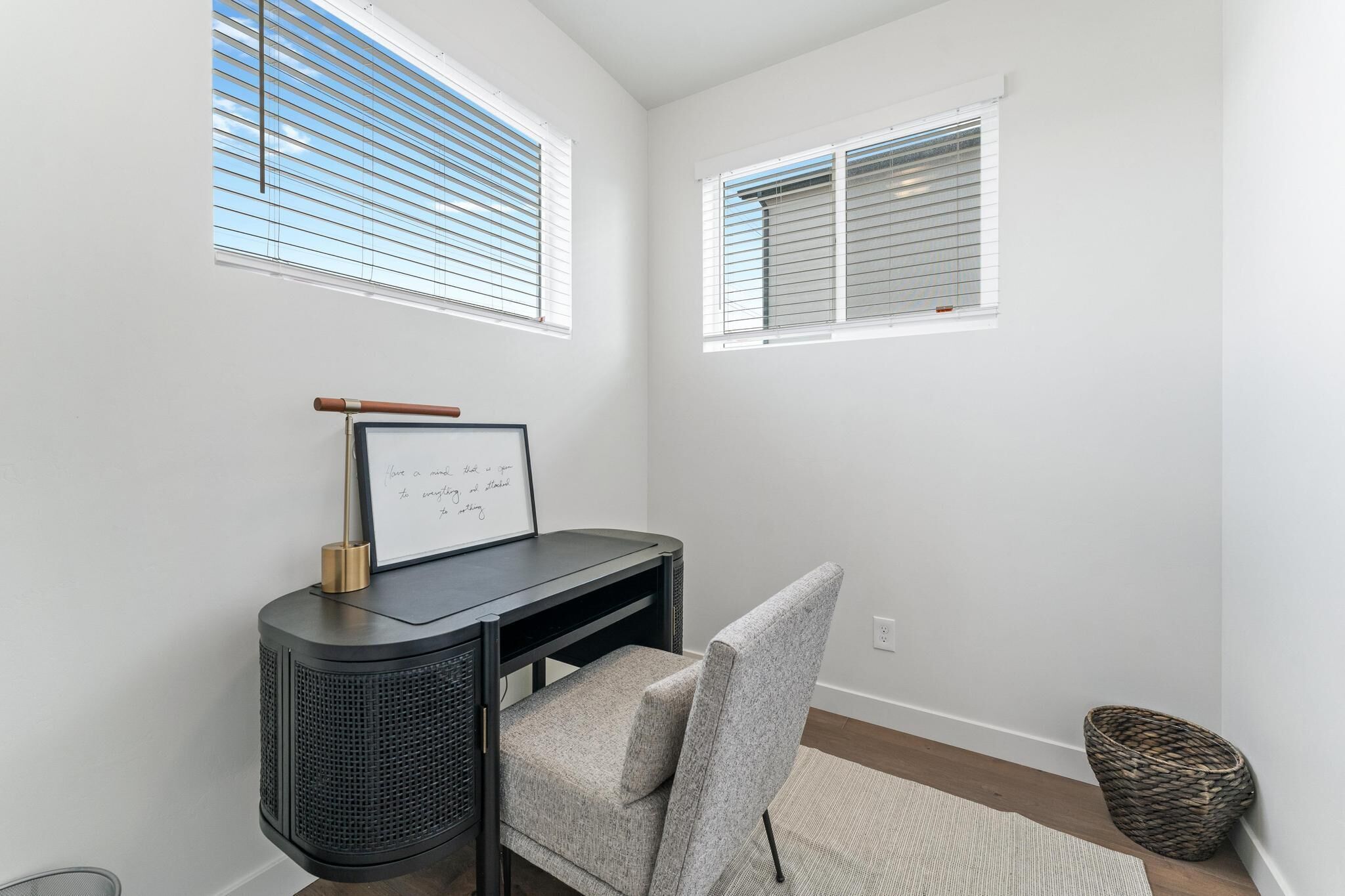 A room with a desk, chair, and two windows with blinds.