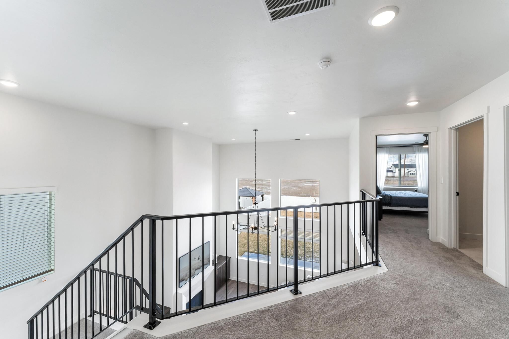 Un intérieur spacieux et bien éclairé, avec un escalier, une vue sur l’extérieur et une porte donnant sur une autre pièce.