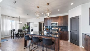 A modern kitchen with a central island, dark wooden cabinets, stainless steel appliances, and pendant lighting. - Home in American Fork - Lakeshore (Highland)