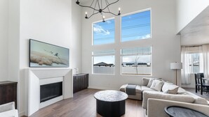 A spacious living room with a fireplace, large windows, a round coffee table, and a sofa. - Home in American Fork - Lakeshore (Highland)
