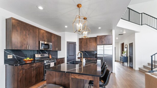 A modern kitchen with dark wood cabinets, stainless steel appliances, and a black marble island. - Home in American Fork - Lakeshore (Highland)