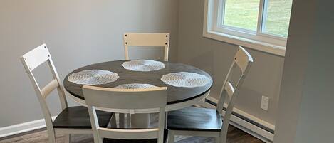 A dining area with a round table, four chairs, and a window with a view of trees.