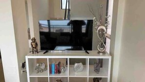 A living room with a flat-screen TV on a white entertainment center, surrounded by shelves with decorative items. - Apartment La Verita, Caleta de Fuste (Castillo Caleta de Fuste)