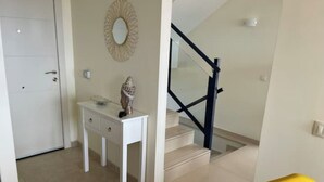 A clean, modern interior with a white door, a small table with a decorative item, a staircase with glass railings, and a yellow chair. - Apartment La Verita, Caleta de Fuste (Castillo Caleta de Fuste)