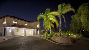A well-lit house with a driveway, palm trees, and a large rock in the front yard. - Private European Vineyard w/ Secluded Hilltop Views in Wine Country (Temecula)