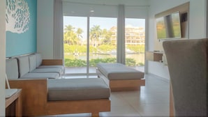 A modern hotel room with a large window, a ceiling fan, a flat-screen TV, and a seating area with a sofa and ottoman. - Pacifika Apartments (Mazatlán)