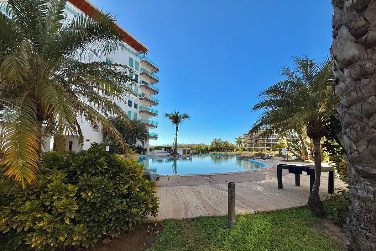 Un complexe hôtelier doté d’une piscine, de palmiers et d’une terrasse en bois.