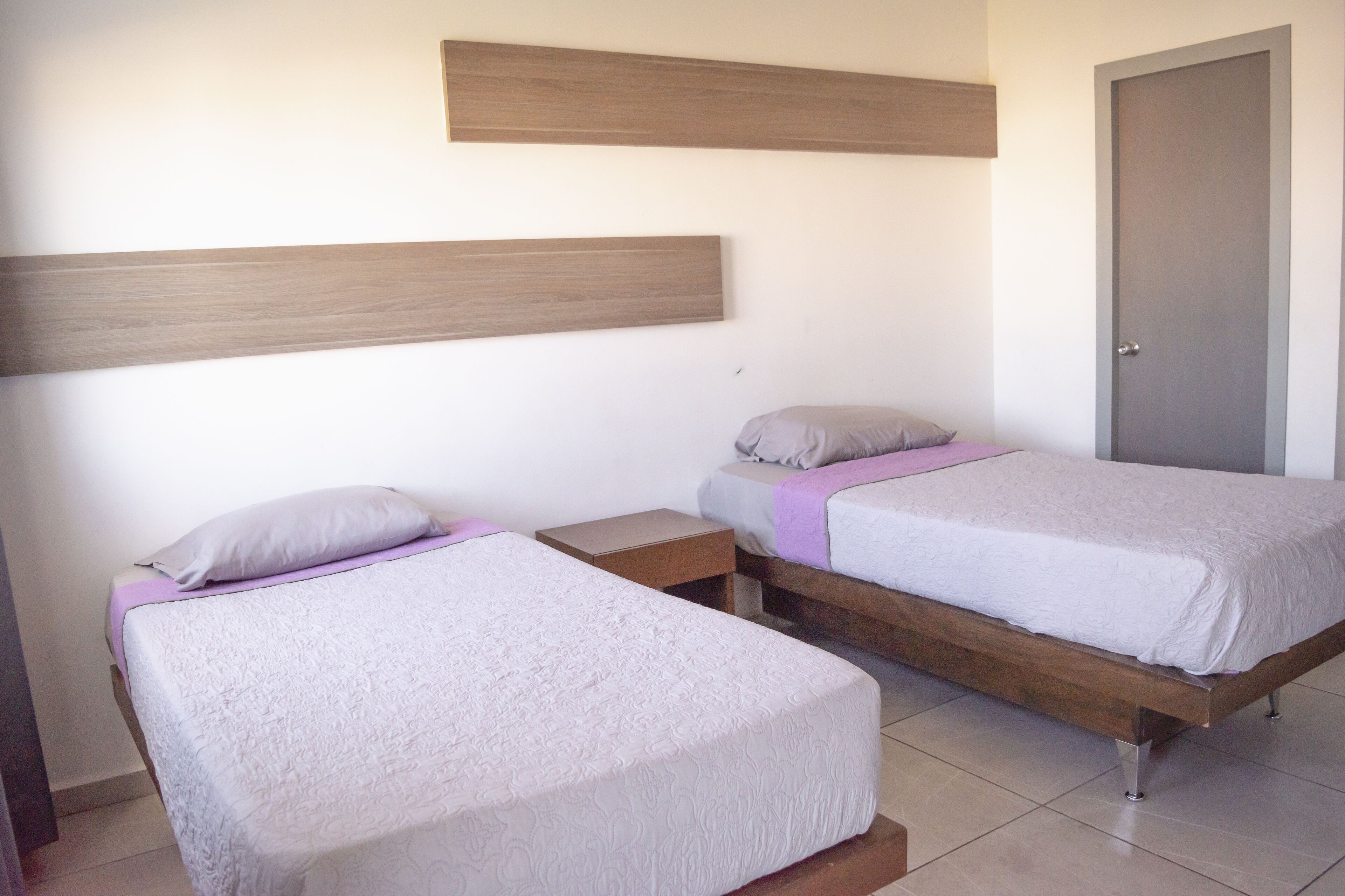 Ein Schlafzimmer mit zwei Einzelbetten, jeweils mit einem Holz-Kopfteil, einem Nachttisch und einer Tür rechts.