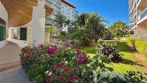 A modern hotel with a covered walkway, lush greenery, and a clear blue sky. - Pacifika Apartments (Mazatlán)