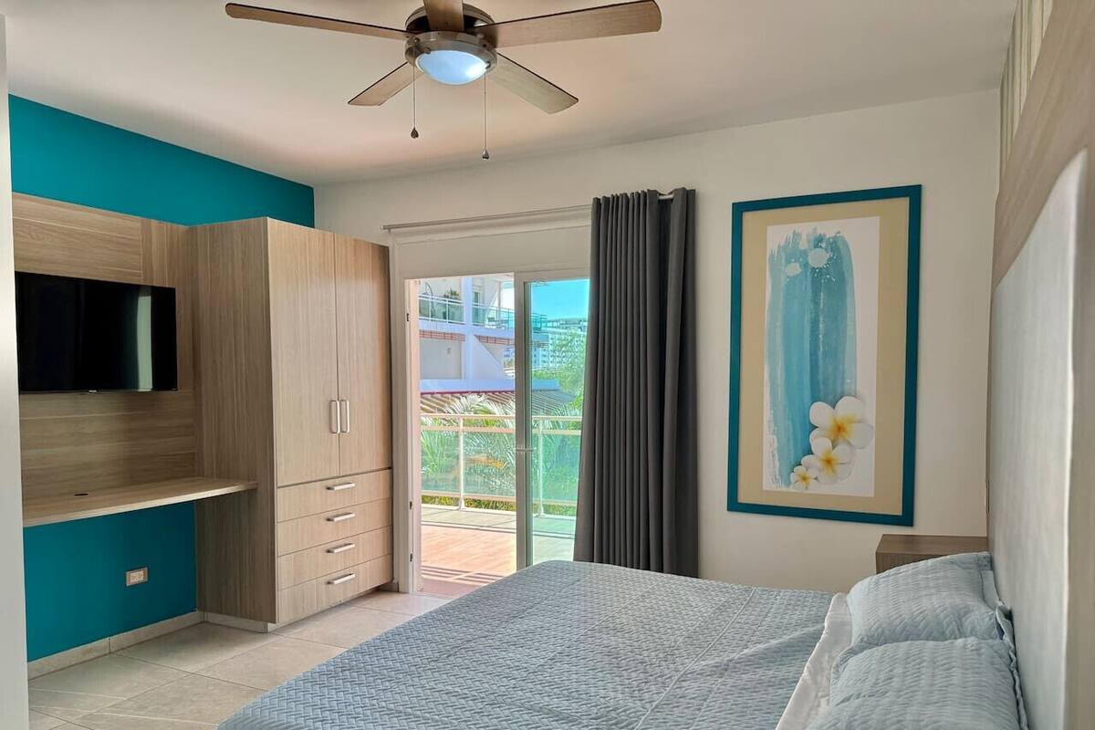 Une chambre à coucher comprenant un lit, une télévision, une armoire et un balcon avec des rideaux.