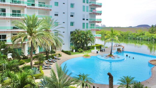 A hotel with a large pool, palm trees, and a view of the water. - Pacifika Apartments (Mazatlán)