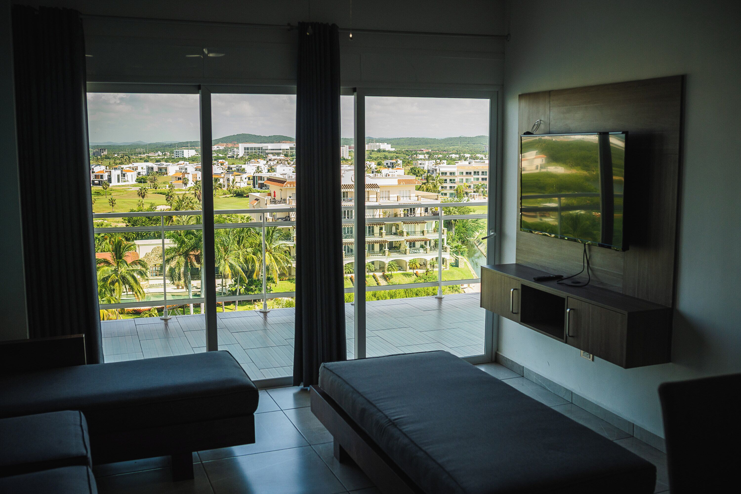 A modern hotel room with a large balcony, a flat-screen TV, and a sofa.