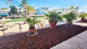 A poolside area with potted plants, a stone bench, and a view of a building with a pool. - Sea Gem-2/2 half duplex with quick ocean access, dockage  (Marathon)