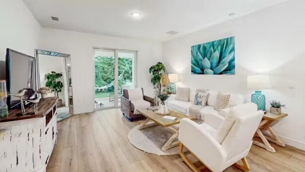 A spacious living room with a white sofa, a coffee table, and a TV on a wooden cabinet. There is a large window with a view of greenery outside. - Boaters Cove ~ 3 Car Garage Home (Sebastian)