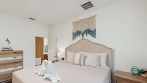 A neatly made bed with a headboard, a wooden dresser, and a wall-mounted tapestry. - Boaters Cove ~ 3 Car Garage Home (Sebastian)